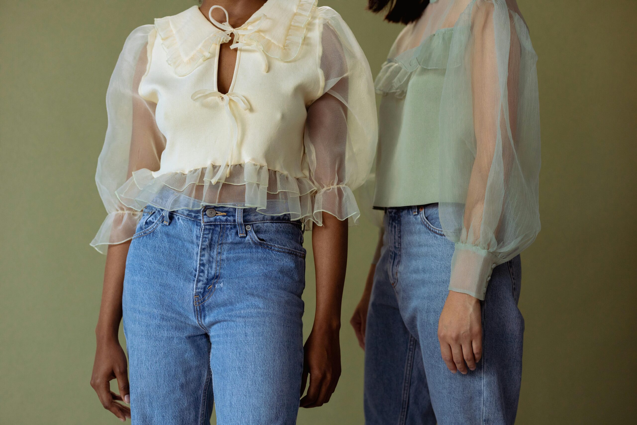 Two women wearing sheer blouses and denim jeans, embodying chic style.
